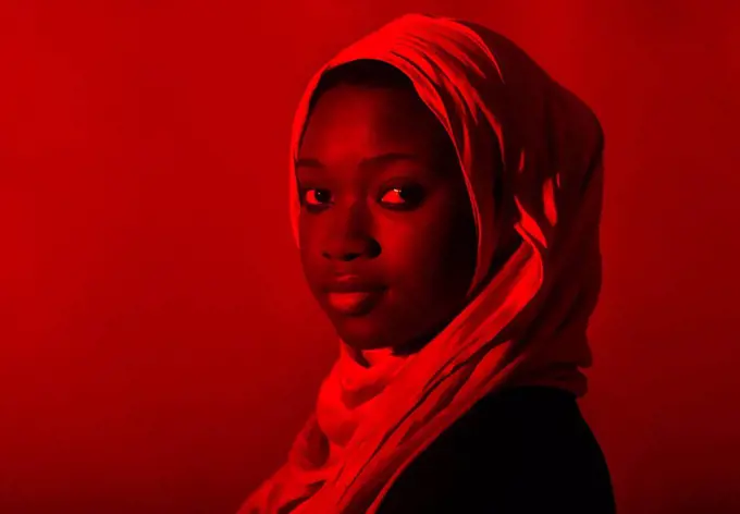 Young woman in hijab staring in front of red background