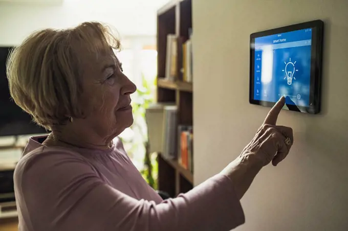 Senior woman touching home automation device on wall