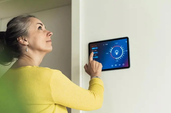 Woman looking away while standing by home automation device on wall