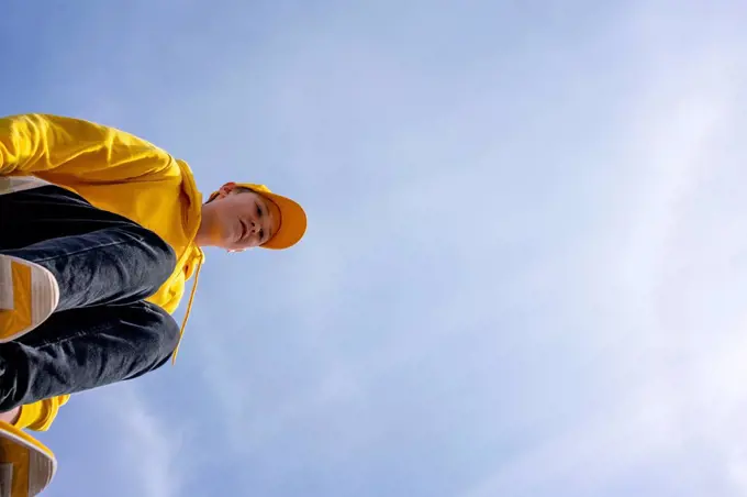 Pre-adolescent boy wearing yellow sweatshirt and cap on sunny day