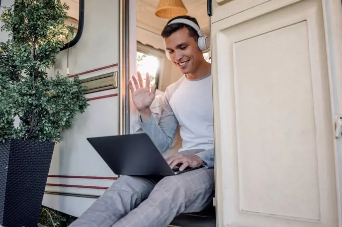 Smiling male freelancer waving hand during video call through laptop