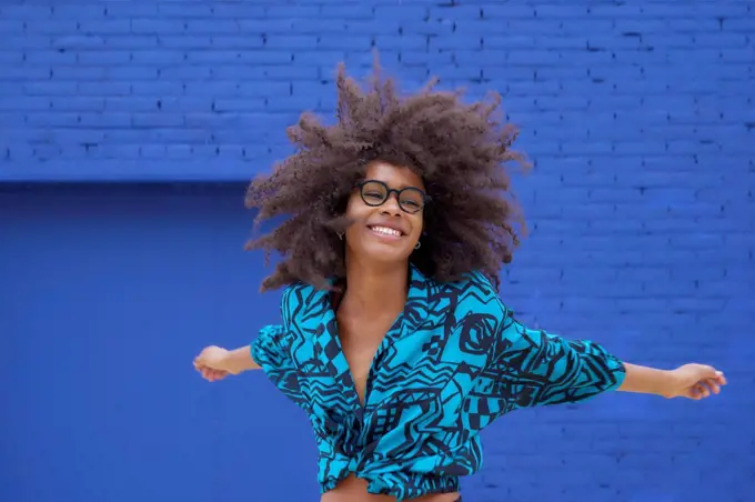 Happy woman dancing with arms outstretched in front of blue wall