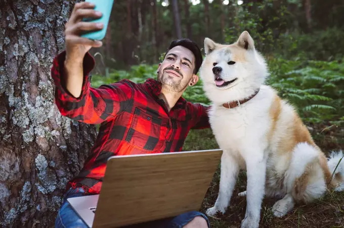 Man taking selfie with dog through mobile phone while sitting at forest