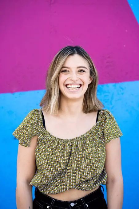 Cheerful young woman smiling in front of colorful wall