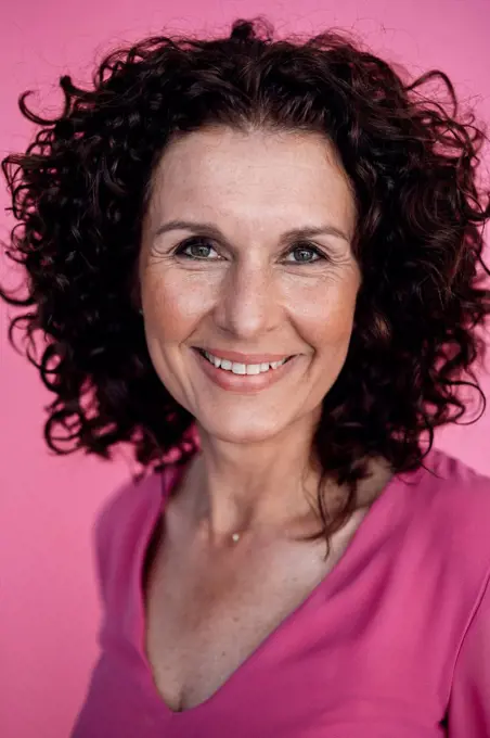Curly haired businesswoman smiling over pink background