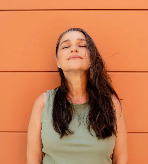 Woman with eyes closed leaning on orange wall