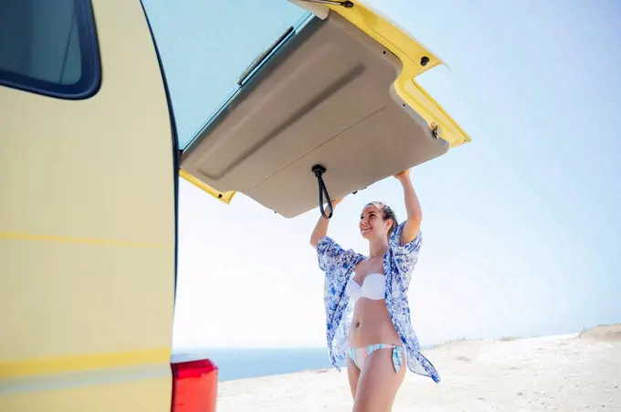Smiling woman closing camper trunk during sunny day