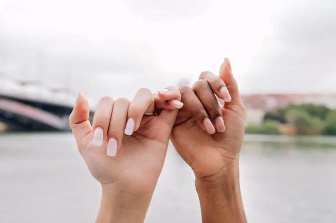 Lesbian couple holding fingers by lake