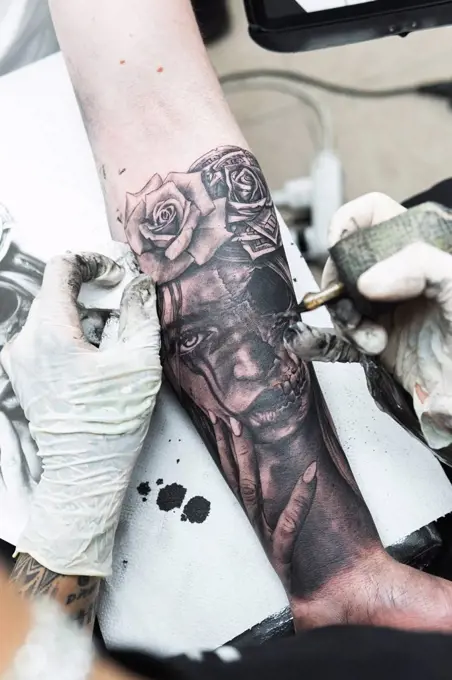 Female artist tattooing on male customer's arm in studio