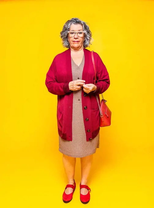 Senior woman with side bag standing in front of yellow background
