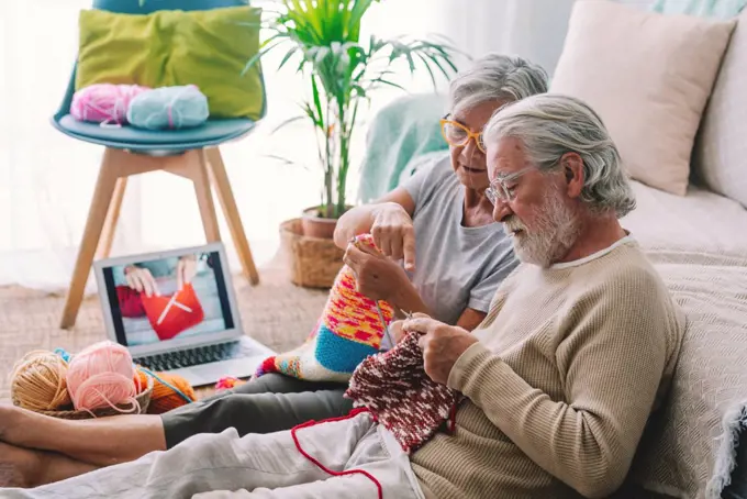Senior woman teaching man to knit wool with needle at home