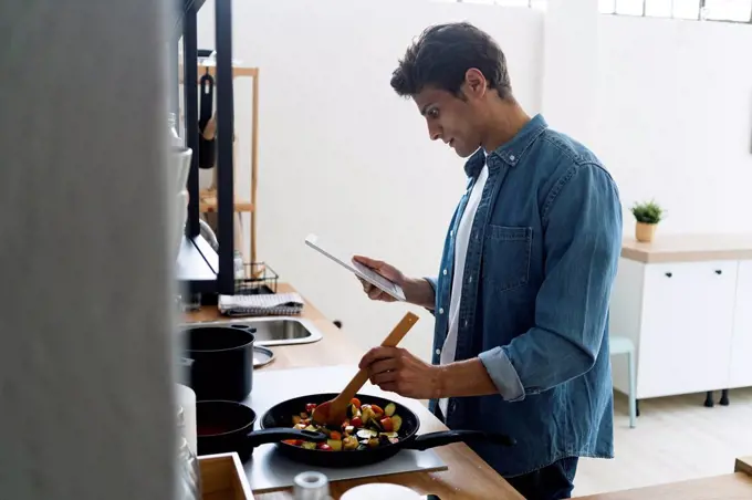 Man using digital tablet while preparing food in kitchen