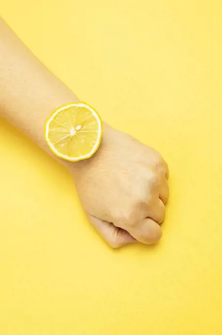 Woman using slice of lemon on wrist against yellow background