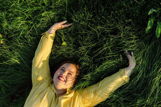 Happy woman with arms raised lying on grass