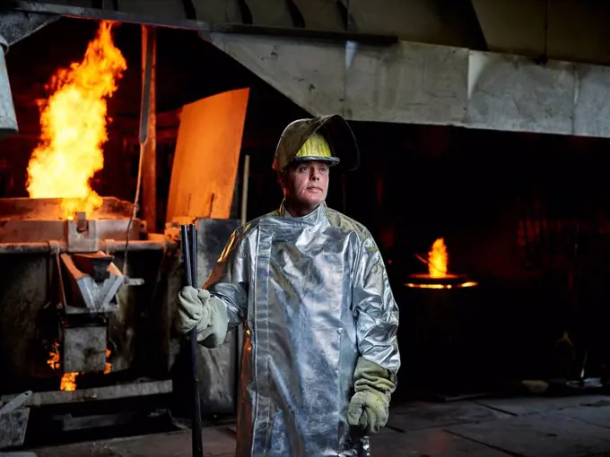 Contemplative blue-collar worker wearing helmet and protective suit in metal industry