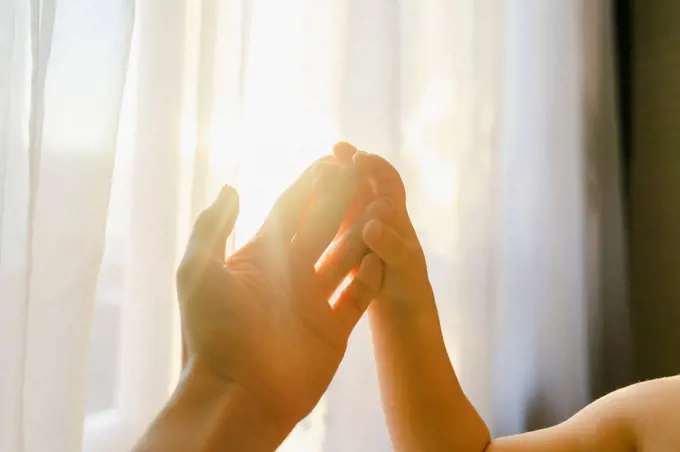 Boy touching mother's hand in front of curtain at home