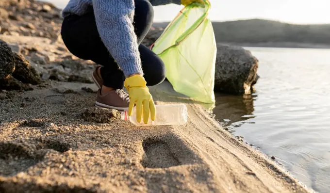 Woman picking up plastic bottle on beach by seashore