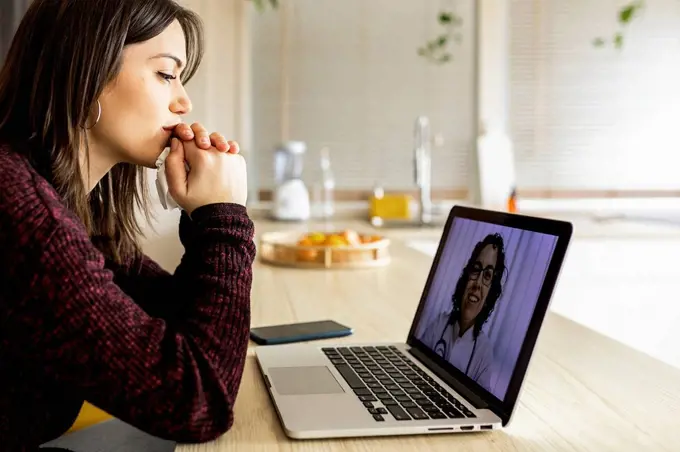Young woman doing online consultation with doctor on laptop at home