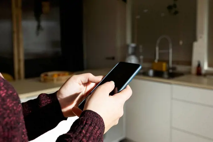Woman using smart phone in kitchen on sunny day