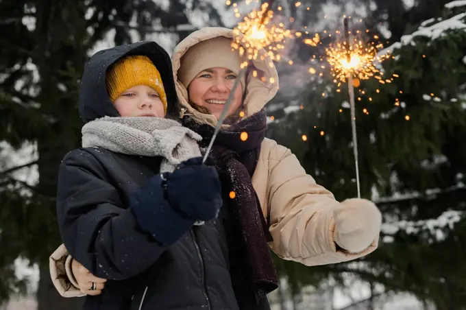 Smiling mother with son looking at sparklers in winter