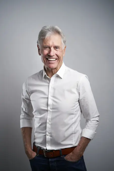 Happy businessman with hands in pockets in front of gray background