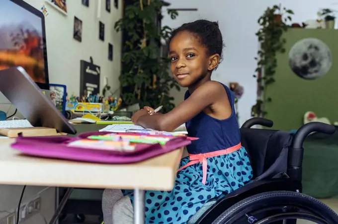 Smiling girl sitting on wheelchair and studying at home