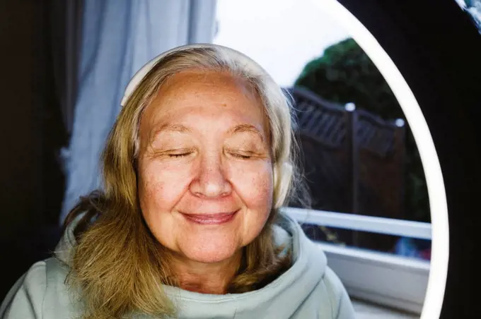 Senior woman with eyes closed seen through illuminated ring light