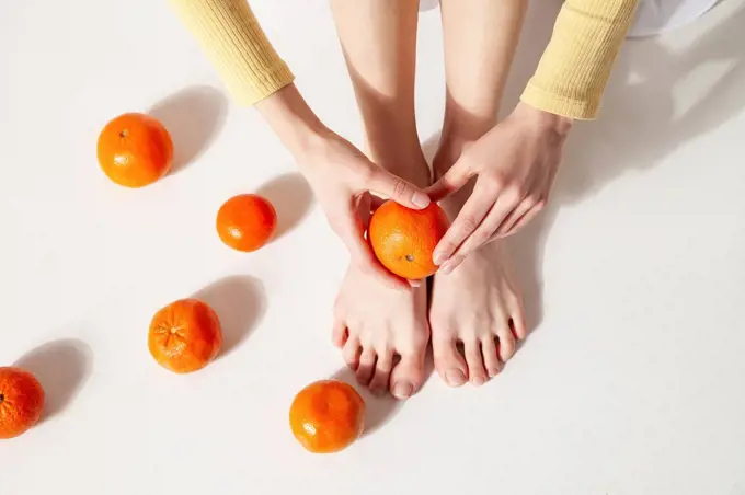 Woman holding tangerine above foot sitting on floor at studio