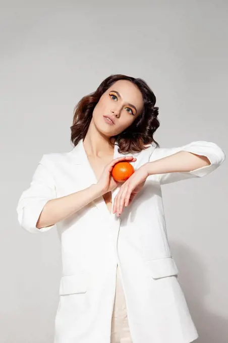 Woman holding tangerine standing against white background