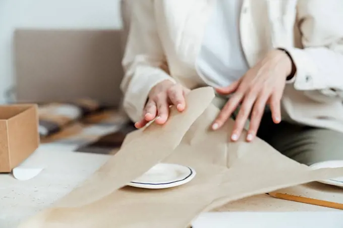 Craftswoman packing ceramic plate in wrapping paper for shipping
