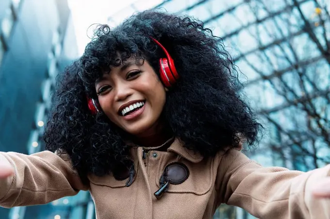 Happy young woman with curly hair listening music through wireless headphones