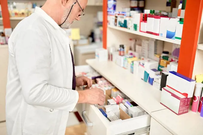 Pharmacist wearing eyeglasses opening drawer of medicines at pharmacy store