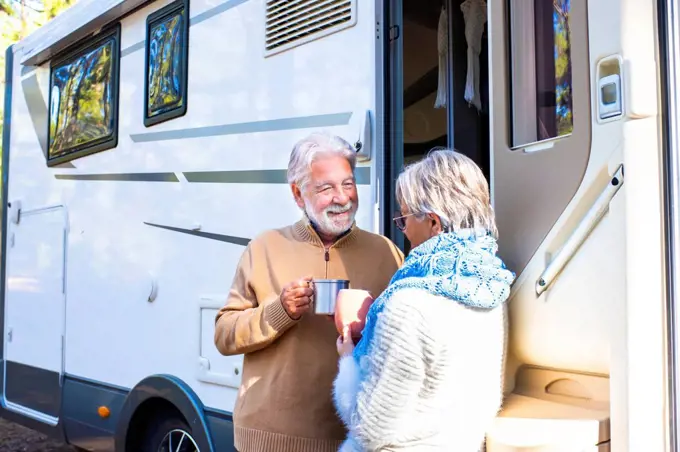 Happy senior couple holding coffee cup talking with woman by motor home