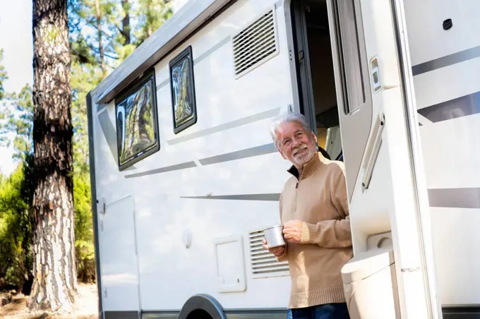Smiling senior man with coffee cup standing at door of motor home