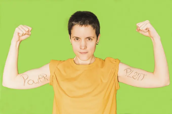 Woman with short hair flexing muscles against green background