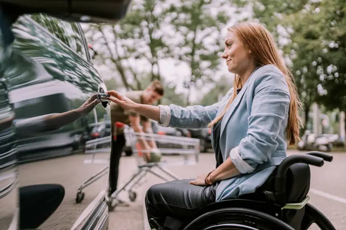 Smiling young woman sitting in wheelchair and opening car door
