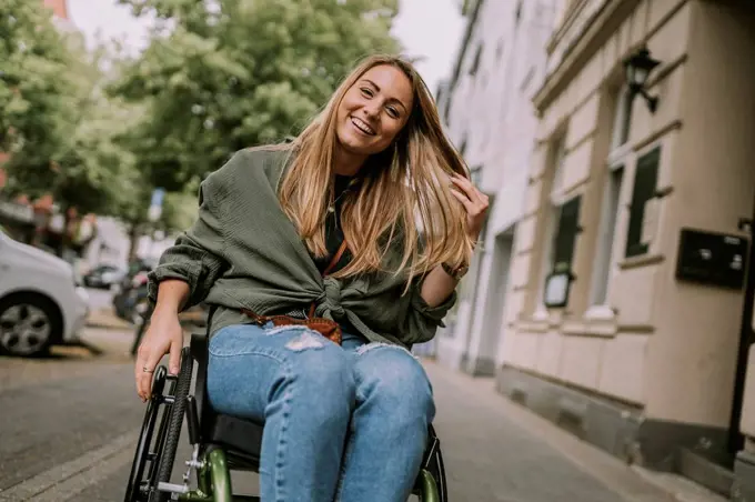 Happy woman sitting in wheelchair at sidewalk