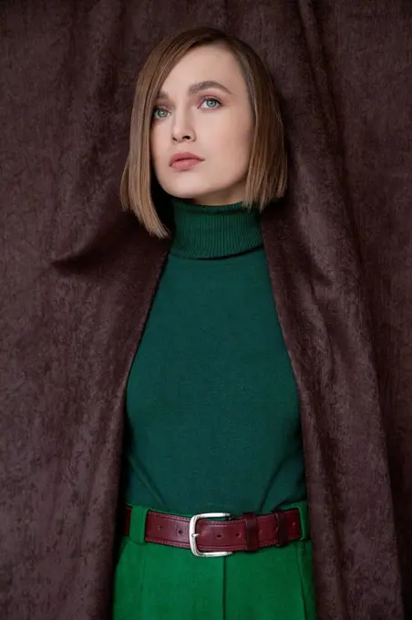 Beautiful woman in green turtleneck top standing amidst curtain