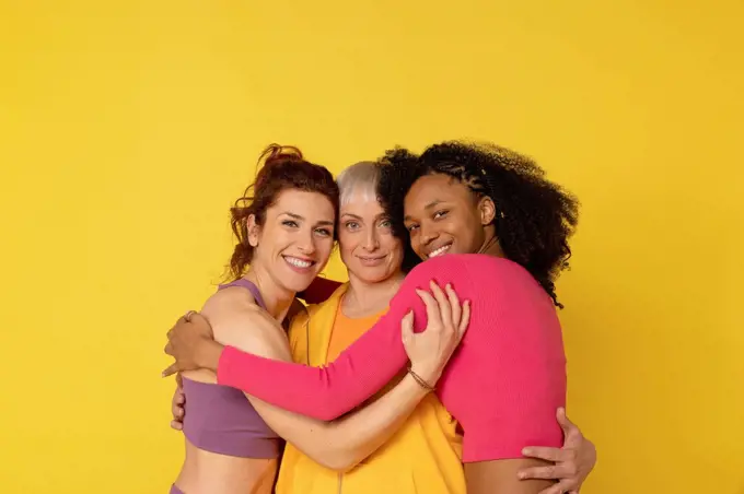 Smiling multiracial friends hugging each other against yellow background