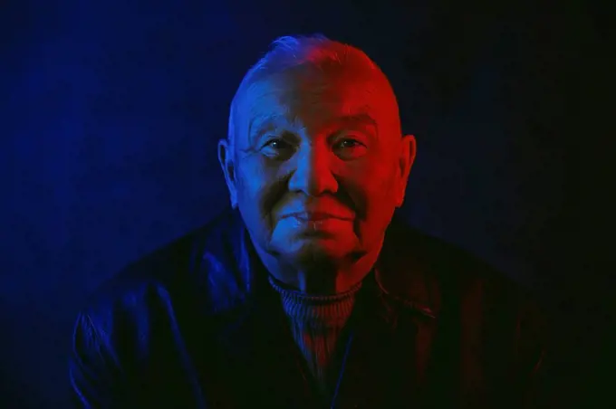 Senior man's face illuminated with red and blue neon light against black background