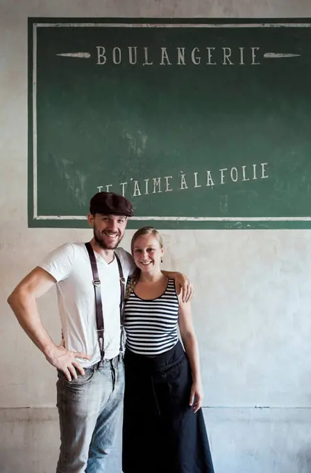 Baker with arm around coworker standing in front of wall with French text