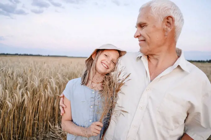 Smiling girl holding crops with grandfather standing at rye field