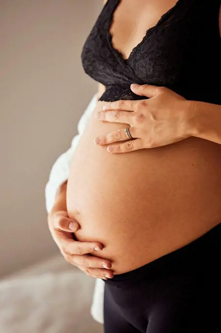 Hands of pregnant woman touching stomach at home