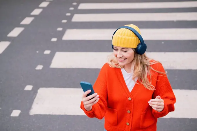 Smiling woman wearing wireless headphones crossing road