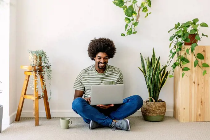 Happy man using laptop sitting in front of wall at home