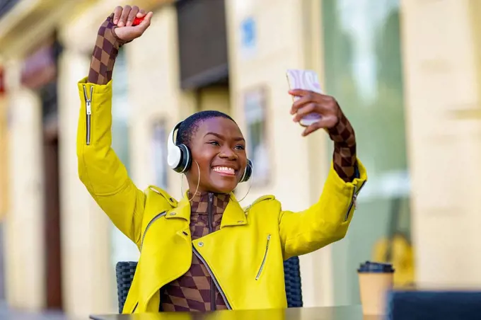 Cheerful woman with hand raised taking selfie through smart phone