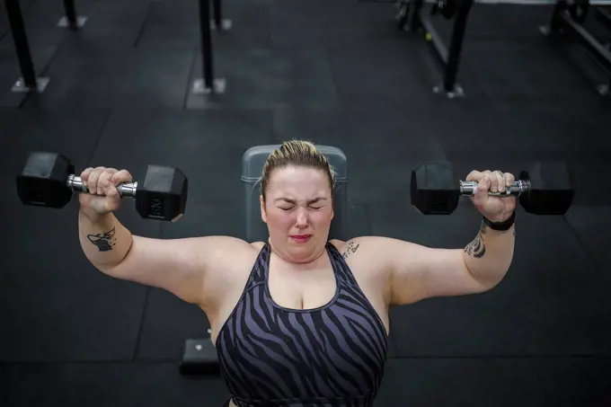 Dedicated overweight woman doing exercise with dumbbells in gym