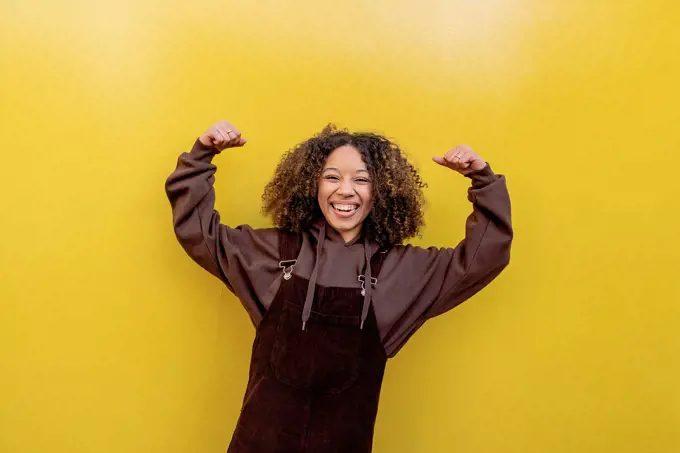 Happy woman flexing muscles in front of yellow wall