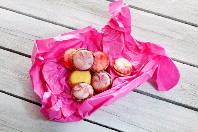 Colorful macarons in pink paper on wood