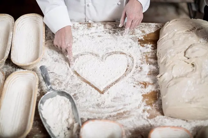 Female baker drawing heart in flour on a wooden table top